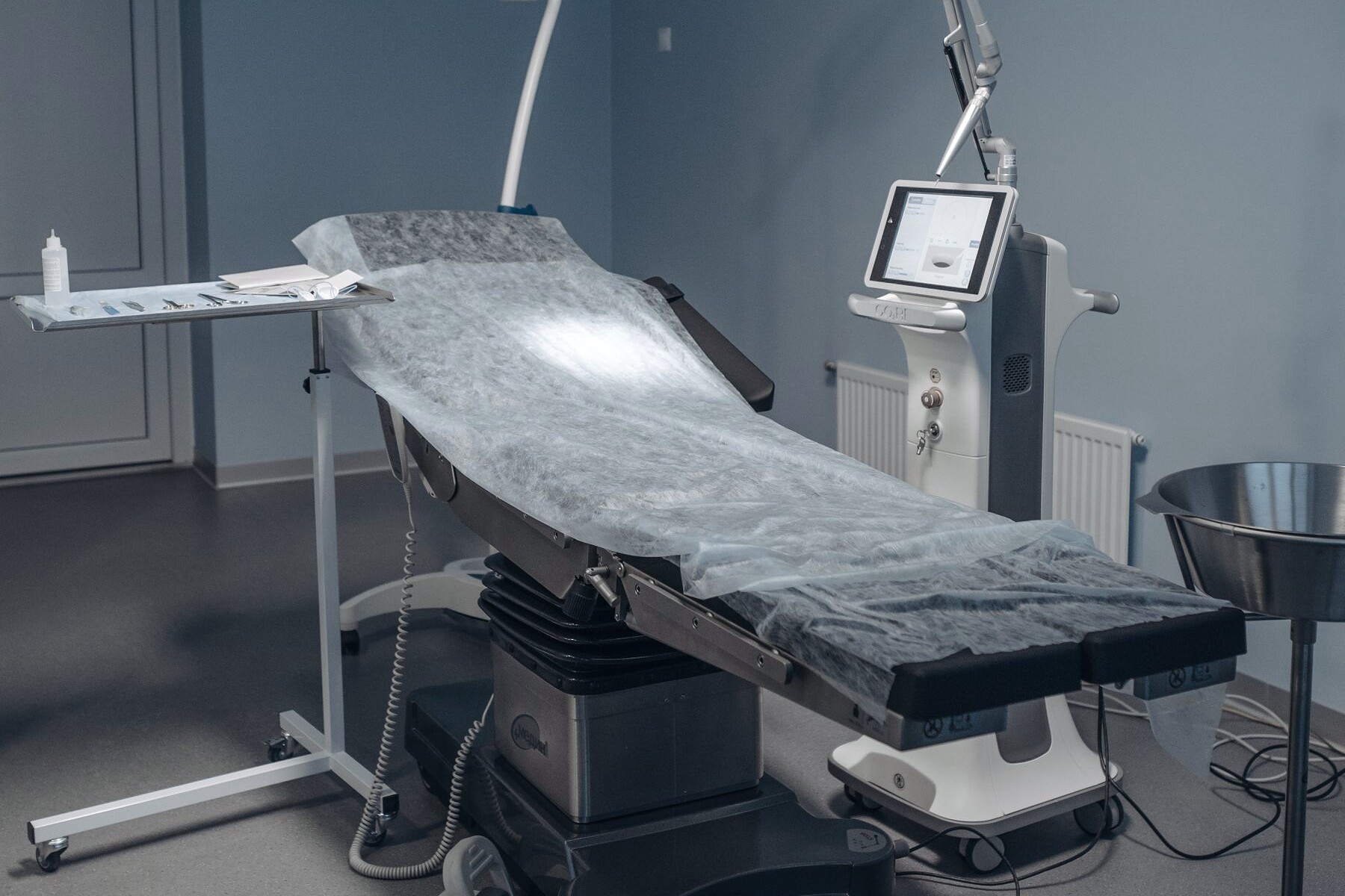 An operating table under a surgical light, draped and set up for a procedure.
